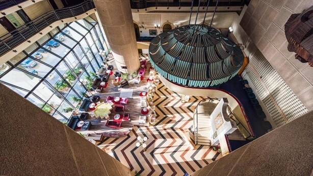 Um amplo átrio com teto alto, uma coluna decorativa central e piso estampado.