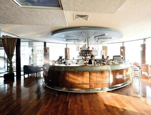 A modern bar area with a curved counter, wooden cabinets, and a ceiling with a unique geometric design. - Hotel Holiday (Sarajevo)