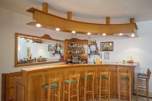 A bar area with wooden bar counter, multiple stools, and shelves stocked with bottles. - Proteas Studios (Naxos)