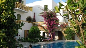 A pool area with a clear view of the pool, a person swimming, and a building with balconies and greenery. - Proteas Studios (Naxos)