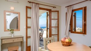 A room with a wooden desk, a small stool, a round table with a fruit basket, and a view of the sea through a window. - Proteas Studios (Naxos)