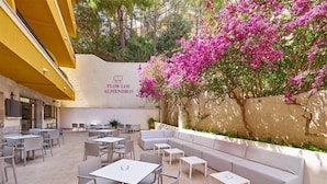 Un espacio al aire libre con mesas, sillas y un sofá, junto a una pared decorada con motivos florales.