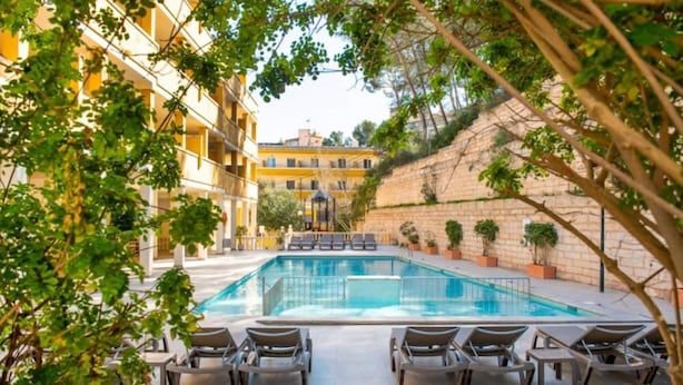 Zona de piscina con sillones de descanso y plantas en macetas, rodeada de edificios.