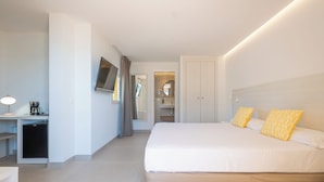 Una habitación de hotel con cama, mesita de noche, lámpara y una pequeña kitchenette.