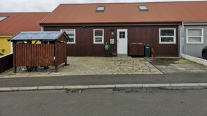 A two-story building with a brown exterior and a red roof. There is a white door with the number 9 above it, and two windows on the upper floor. A small wooden structure is in front of the building. - Rose Cottage 15m2 Tórshavn with Parking (Hoyvík)