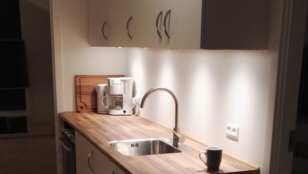 A modern kitchen with a wooden countertop, stainless steel sink, and a coffee maker. - Rose Cottage 15m2 Tórshavn with Parking (Hoyvík)