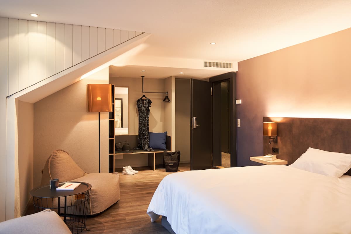 A hotel room with a bed, a seating area with a table, a wardrobe, and a staircase.