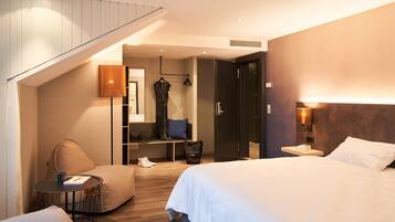 Une chambre d’hôtel comprenant un lit, un coin salon avec une table, une armoire et un escalier.