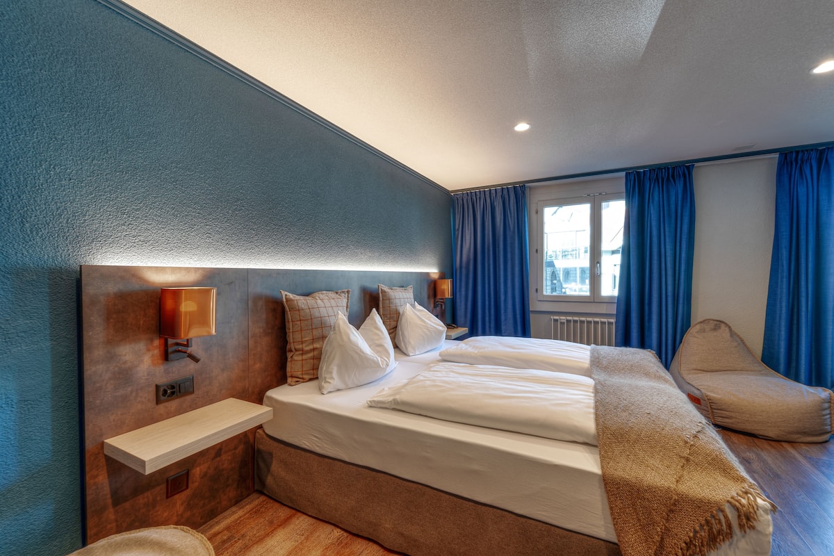 A hotel room with a large bed, bedside tables, a chair, and a window with curtains.