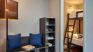 A room with a bunk bed, a bookshelf, a desk with a lamp, and a pair of blue pillows.