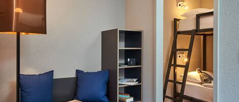 A room with a bunk bed, a bookshelf, a desk with a lamp, and a pair of blue pillows.