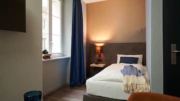 Una habitación de hotel con cama, mesita de noche, lámpara y ventana con cortinas.