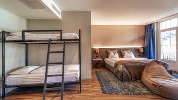 Hotelkamer met stapelbedden, een los bed, nachtkastje, lamp, raam met gordijnen en een kamerbreed tapijt met patroon.