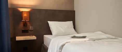 A hotel room with a bed, a nightstand with a lamp, a wine glass, and a camera.