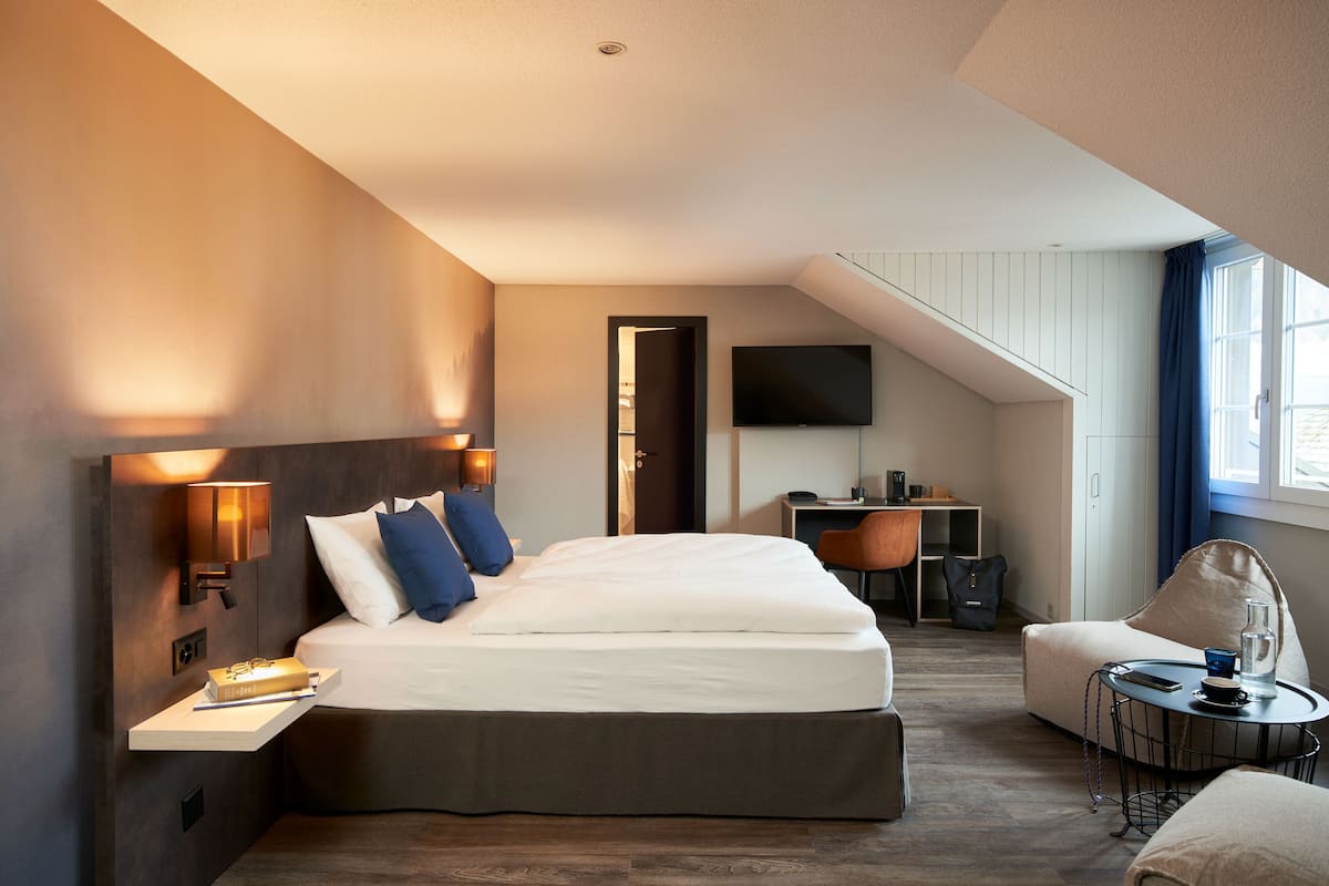 A modern hotel room with a large bed, a desk, a chair, and a TV mounted on the wall.