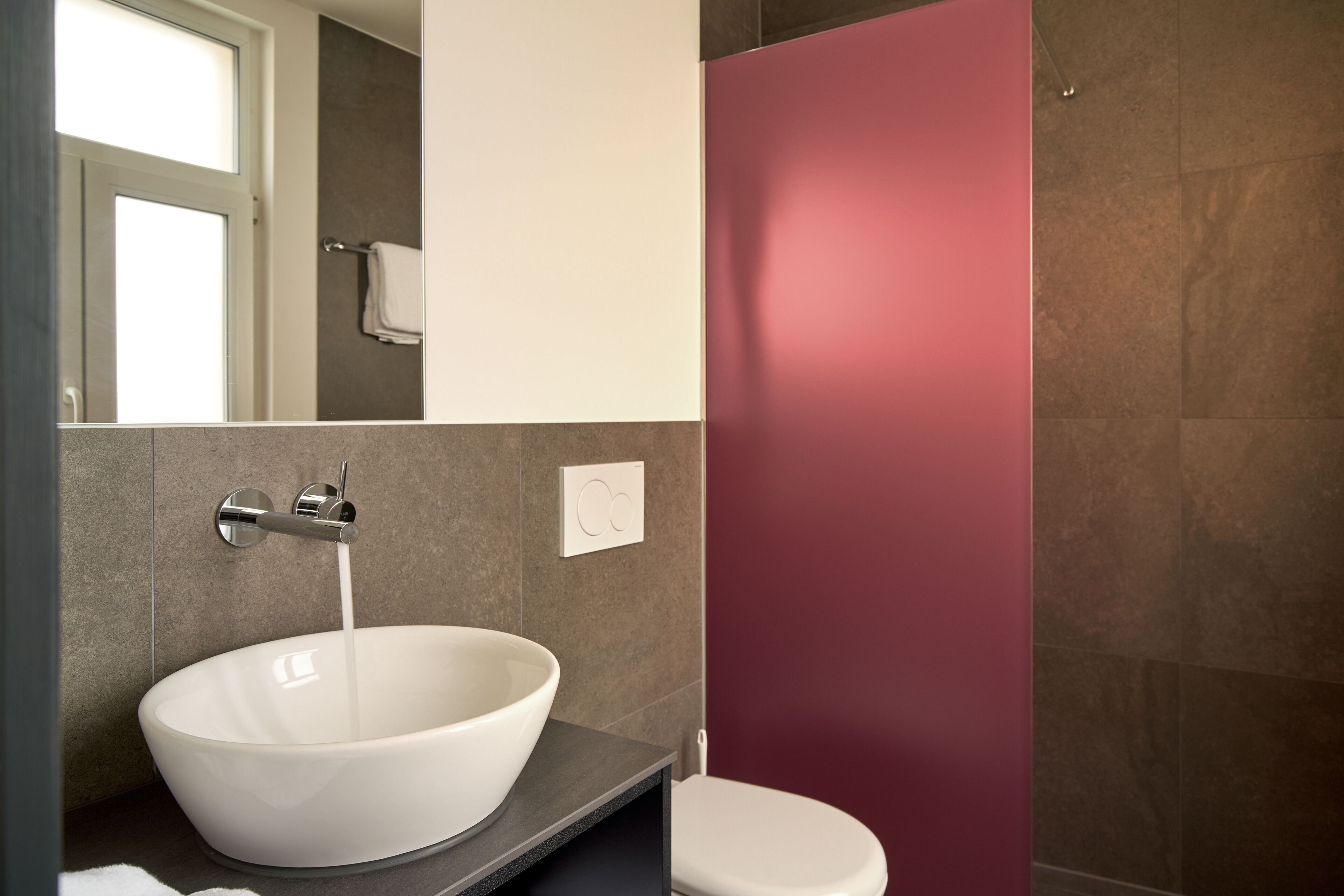 A modern bathroom with a large white vessel sink, a toilet, and a red accent wall.