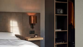 A modern hotel room with a bed, a bedside table with a lamp, a shelf with a radio, and a wardrobe.