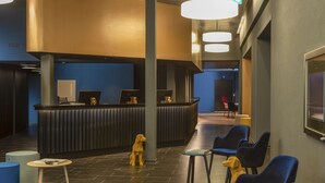 Un área de recepción con mostrador, sillas azules, una pequeña mesa y una estatua de perro.