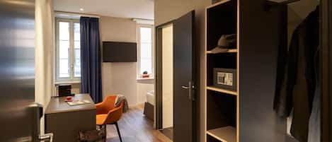 A compact hotel room with a desk, chair, wardrobe, and a TV mounted on the wall.