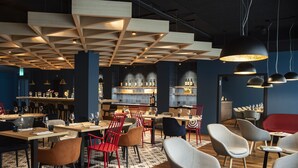Un interior de restaurante moderno con paneles de techo de madera, varias áreas de estar y una barra con estantes llenos de botellas.