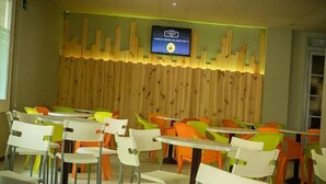 A dining area with colorful chairs and tables, a wooden wall with a mounted television, and a cityscape design. - Sun Beach (Lloret de Mar)