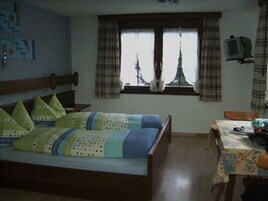 Un dormitorio con cama, escritorio, silla, televisor y ventana con cortinas.