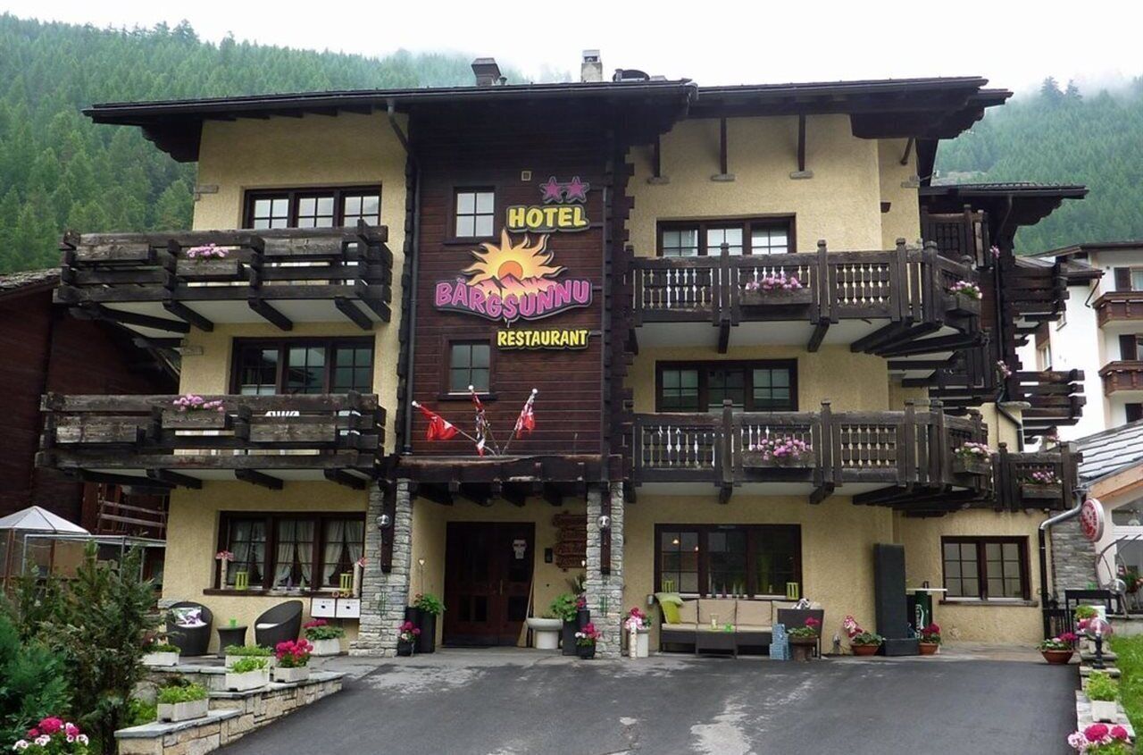 Un albergo con un cartello che riporta la scritta "BARGSUNNU HOTEL RESTAURANT". Presenta balconi in legno e una facciata in pietra.