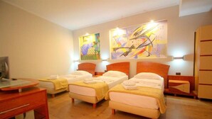 Una habitación de hotel con tres camas individuales, un escritorio y un televisor.