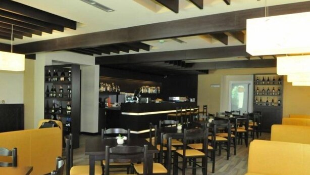 A restaurant with yellow booths and tables, a bar area with a counter, and shelves with bottles. - Sokrat Hotel (Tirana)