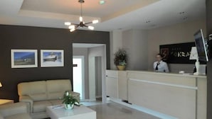 A modern hotel lobby with a reception desk, a sofa, a coffee table, and a ceiling fan. - Sokrat Hotel (Tirana)