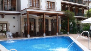 Una piscina con fuente de agua, rodeada de mobiliario exterior y un patio cubierto.