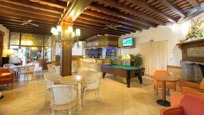 Un espacio interior amplio con mesa de billar, varios conjuntos de asientos, zona de bar y televisor montado en la pared.