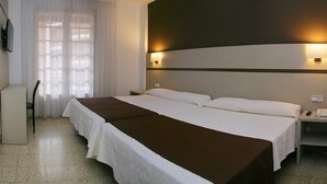 Habitación de hotel con una cama grande, un escritorio y una silla. Hay una ventana con cortinas, una lámpara de pared y un teléfono en la mesita de noche.