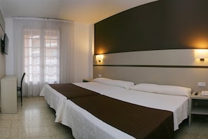 A hotel room with a large bed, a desk, and a chair. There is a window with curtains, a wall-mounted lamp, and a phone on the nightstand. - La Carolina (Lloret de Mar)