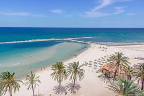Een strand met helder turquoise water, een zandstrand en palmbomen.