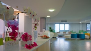 A modern reception area with a counter, orchid vases, and a seating area with colorful chairs. - Relaxia Lanzaplaya (Tías)