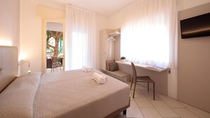 Habitación de hotel con cama, escritorio, silla, televisor y ventana con cortinas.