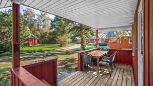A wooden deck with a table and chairs, overlooking a grassy area with red buildings in the background.