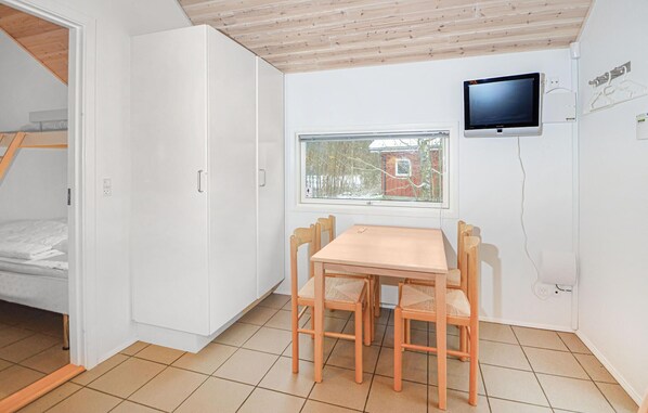 A compact room with a wooden table and chairs, a television mounted on the wall, and a window with a view of a red building.