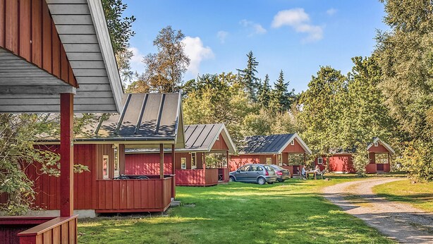 A row of red cabins with a grassy lawn and a dirt path leading to them.