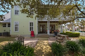 A green house with a porch, outdoor seating, and a lawn.