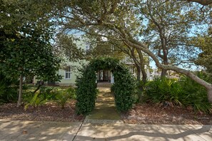 A pathway leading to a building with a covered entrance, surrounded by lush greenery and trees.