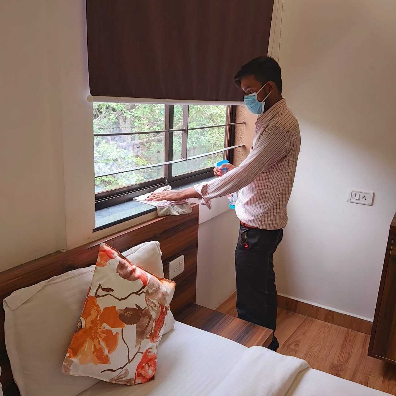 Une personne est en train de nettoyer une fenêtre dans une pièce où se trouvent un lit et un oreiller.