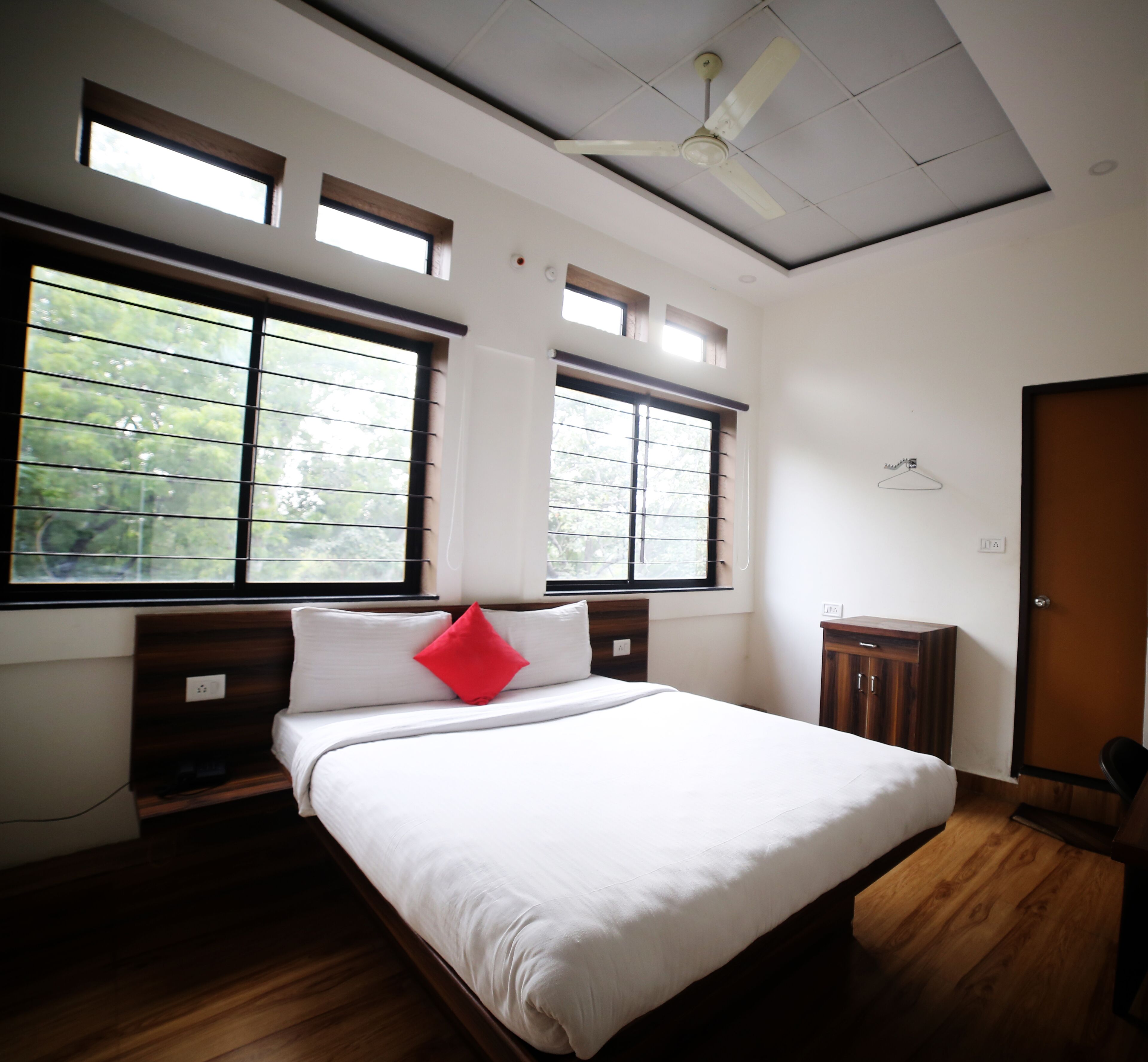 A bedroom with a bed, two windows, a ceiling fan, and a wooden wardrobe.