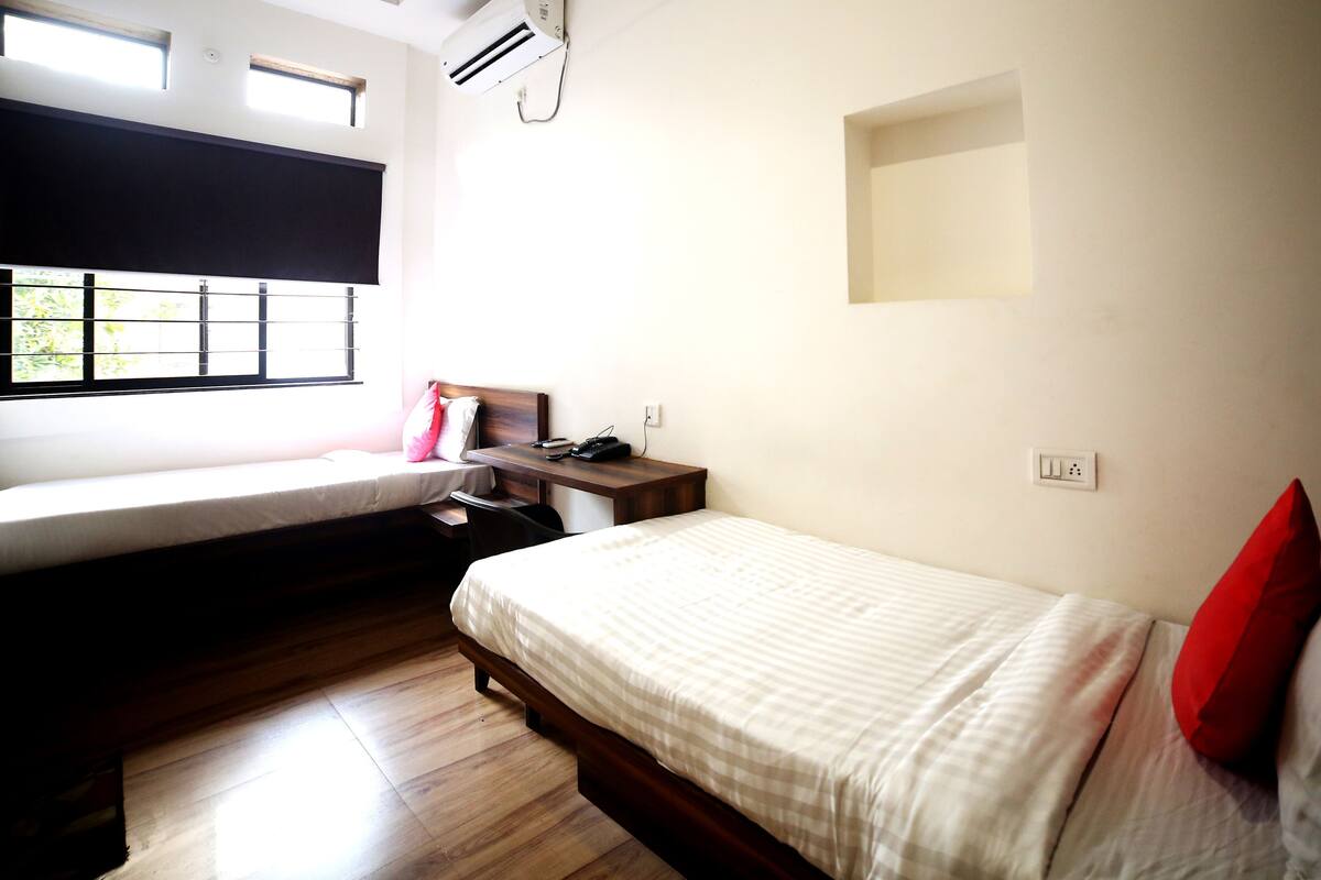 A room with a bed, a desk, a chair, a window with a view, and an air conditioning unit.