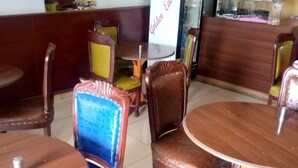 A restaurant interior with wooden tables and chairs, a counter, and a refrigerator. - Golden Bay Hotel (Naivasha)