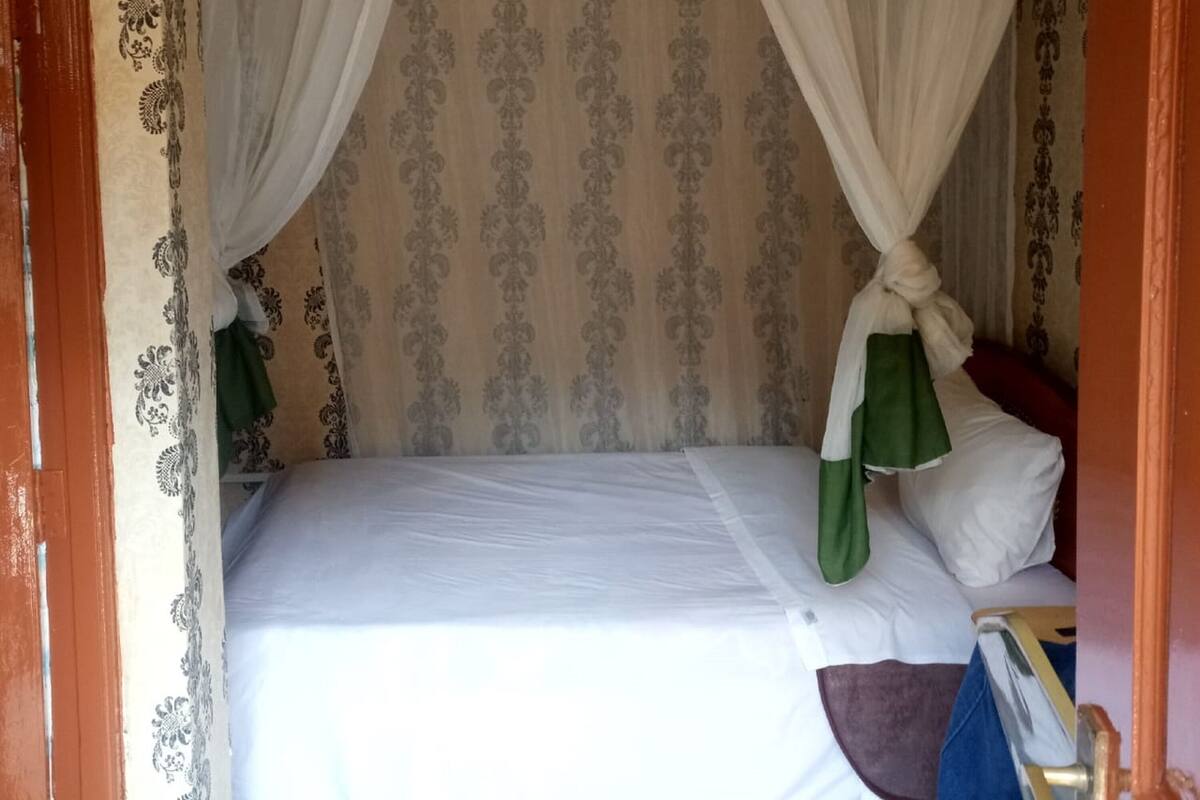 Un lit simple avec un baldaquin, une table de chevet et un papier peint à motifs.