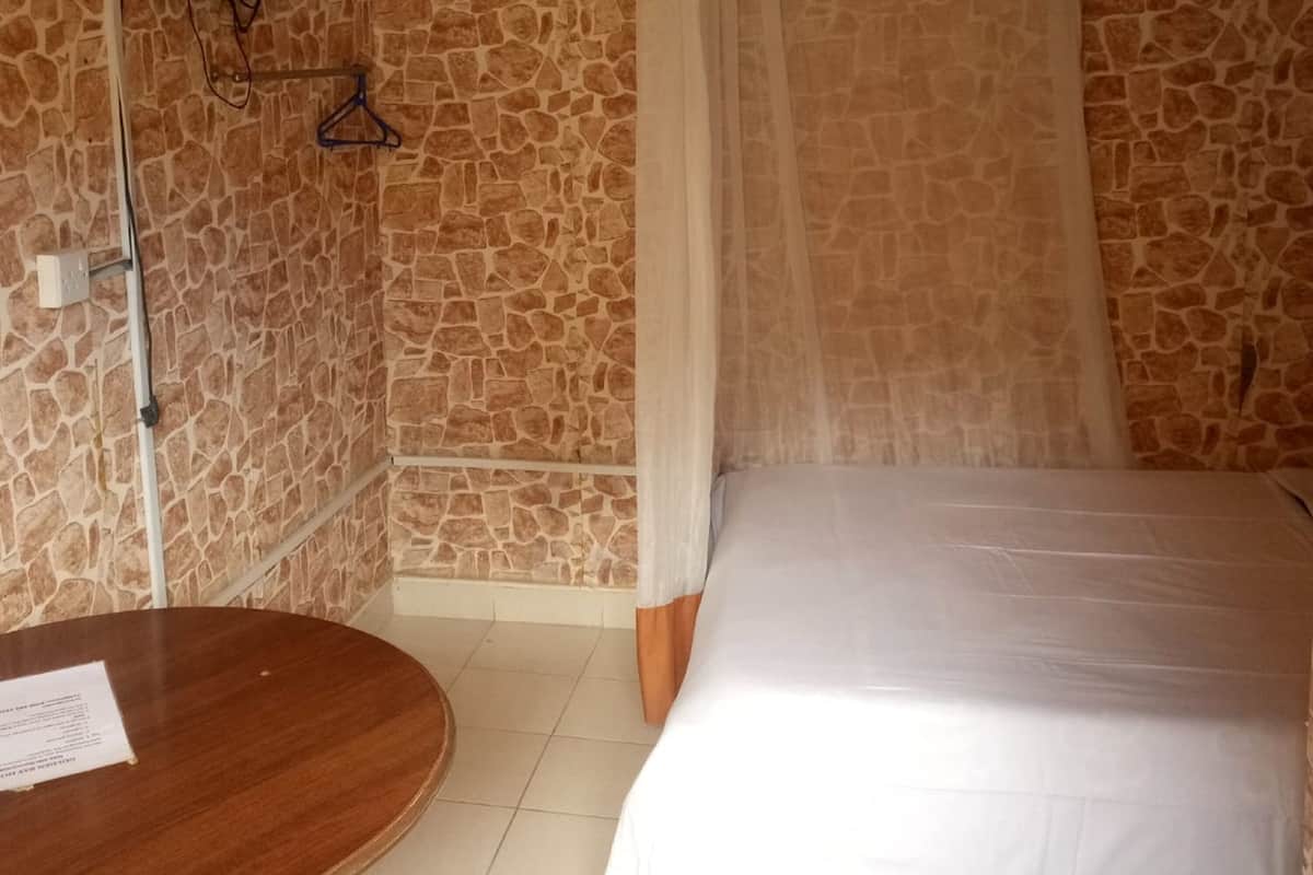Une pièce avec un mur décoré d’un motif en pierre, un lit à baldaquin blanc, une table en bois et un porte-manteau suspendu.