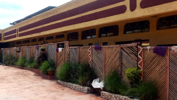 A train station with a yellow building, multiple windows, and a covered waiting area with plants. - Golden Bay Hotel (Naivasha)