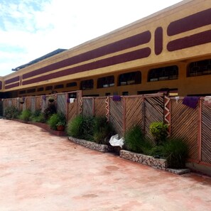 A train station with a yellow building, multiple windows, and a covered waiting area with plants. - Golden Bay Hotel (Naivasha)